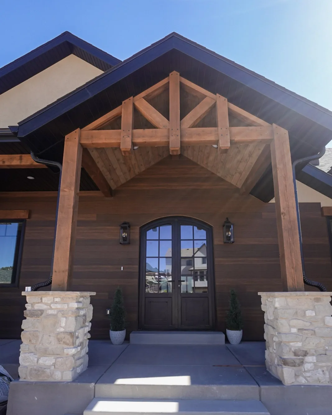 Timber truss entry with stacked stone columns and an arched alder front door