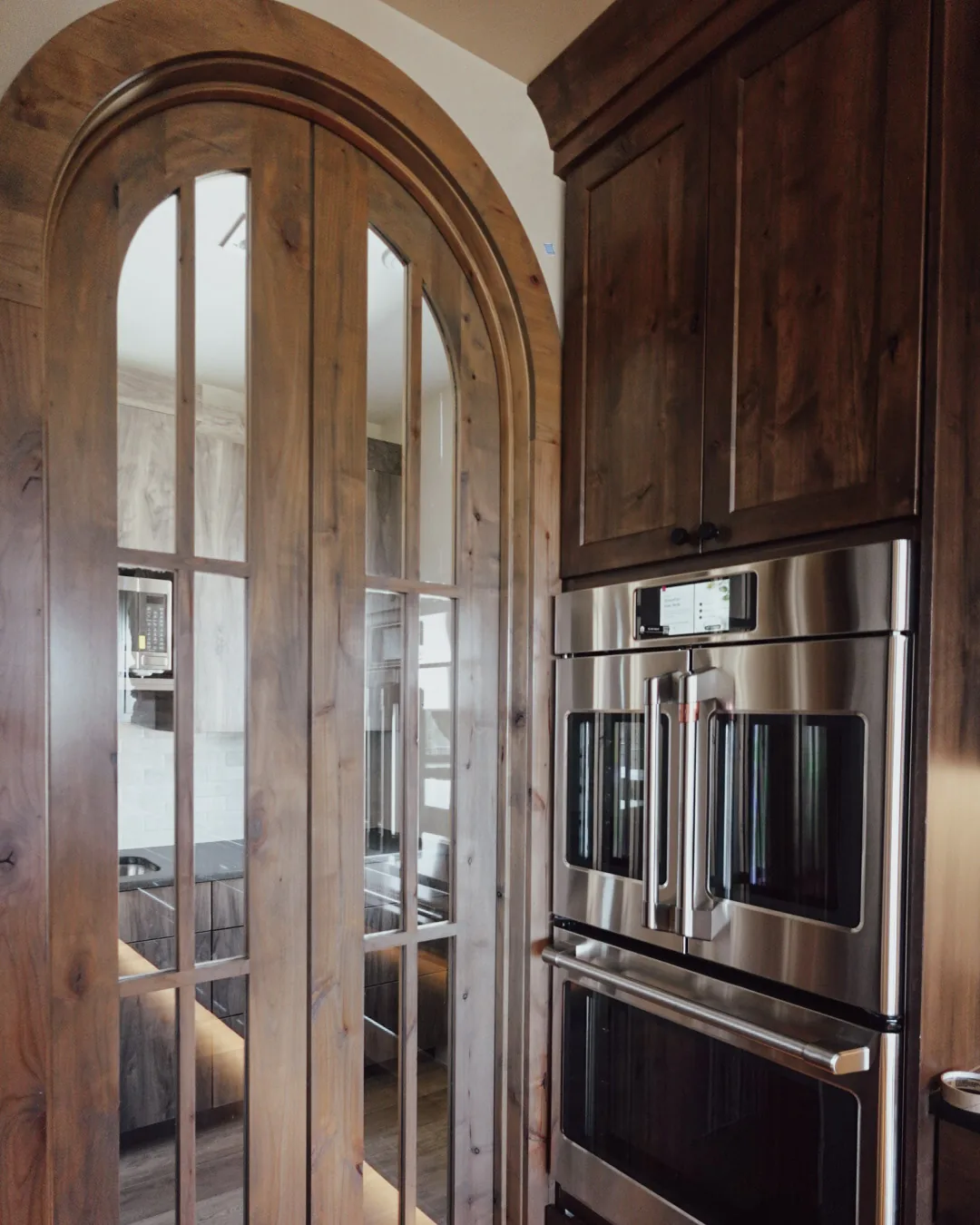 Arched alder door beside a built-in double wall oven